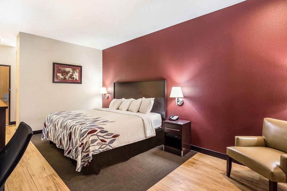 A hotel room with a bed, bedside tables, a chair, and a painting on the wall.