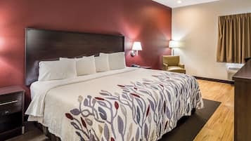 A hotel room with a large bed, a nightstand, a chair, and a desk with a lamp.