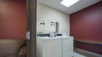 A laundry room with two washing machines, a drying rack, and instructional posters on the wall.