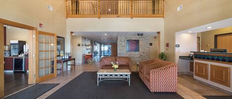 A spacious lobby with a high ceiling, a chandelier, a seating area with patterned sofas, and a vending machine.