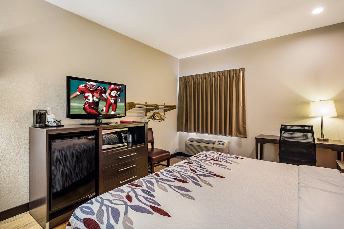 A hotel room with a bed, a desk with a computer, a television, and an air conditioning unit.