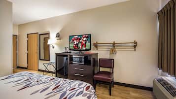 Ein Hotelzimmer mit einem Bett, einem Schreibtisch mit Fernseher, einem Sessel, einer Schreibtischlampe und einem an der Wand befestigten Schlüsselhalter.