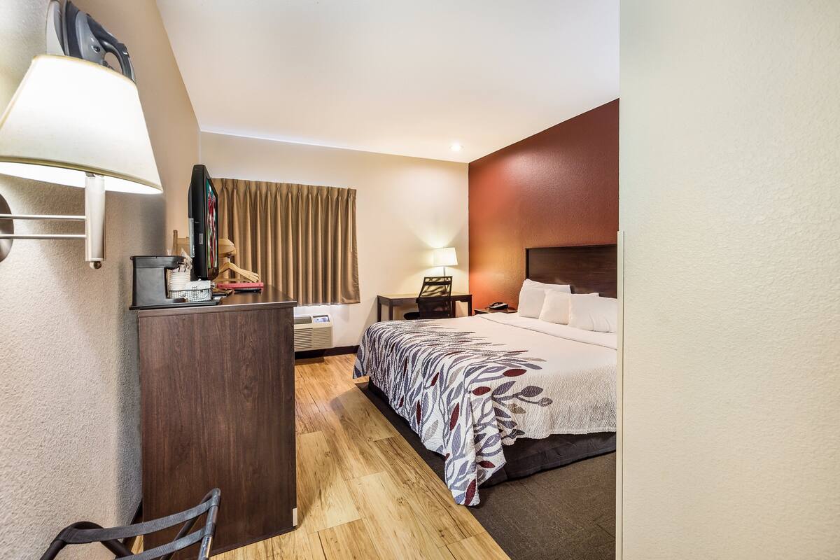 Ein Hotelzimmer mit Bett, Schreibtisch, Stuhl, Lampe und Fernseher.