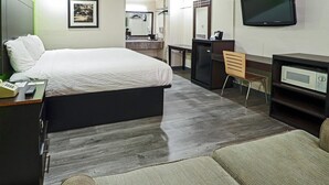 A hotel room with a large bed, a desk, a chair, a TV, and a microwave.