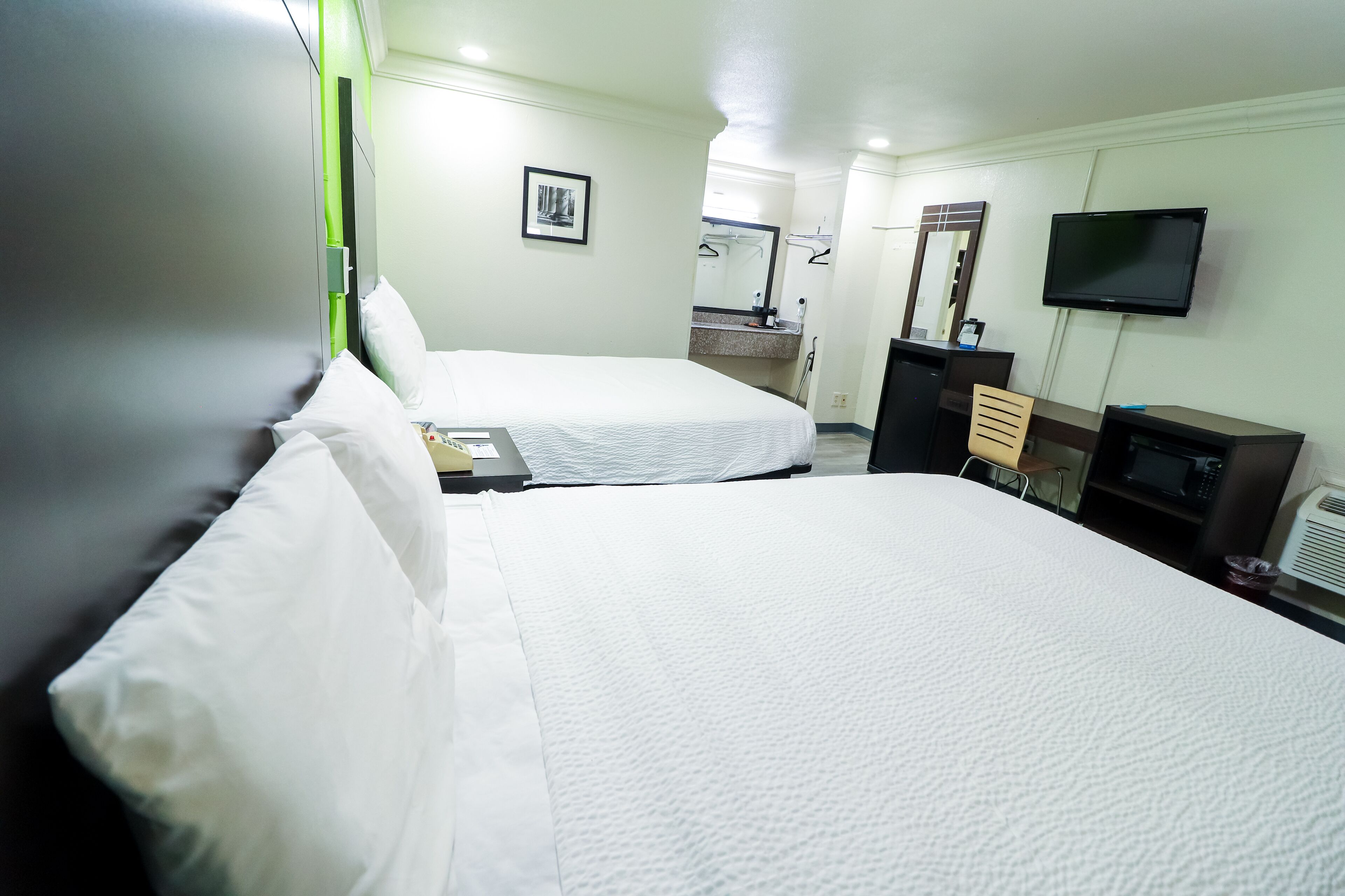 A hotel room with two beds, a TV, a microwave, and a desk.