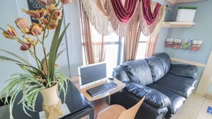 A living room with a black leather sofa, a wooden chair, a laptop on a desk, and a potted plant.