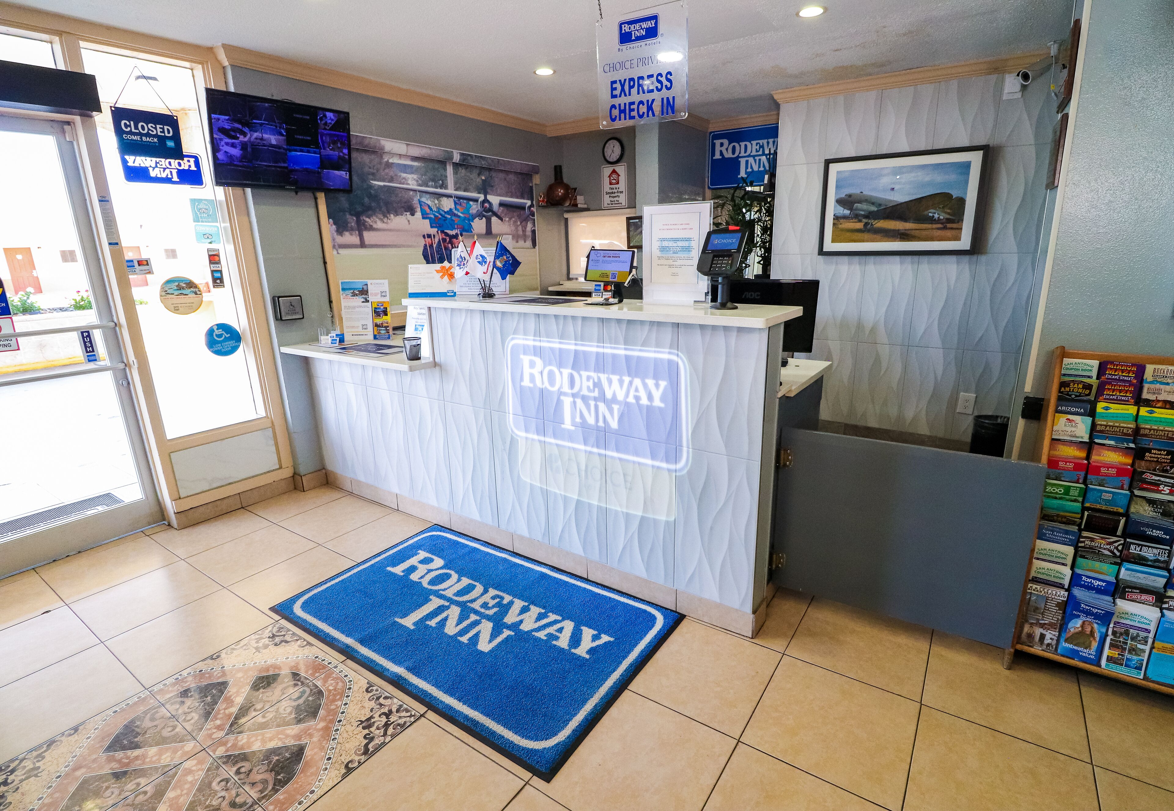A reception area with a 'Rodeway Inn' sign, a digital screen, a clock, and a 'Choice PIN EXPRESS CHECK IN' sign.