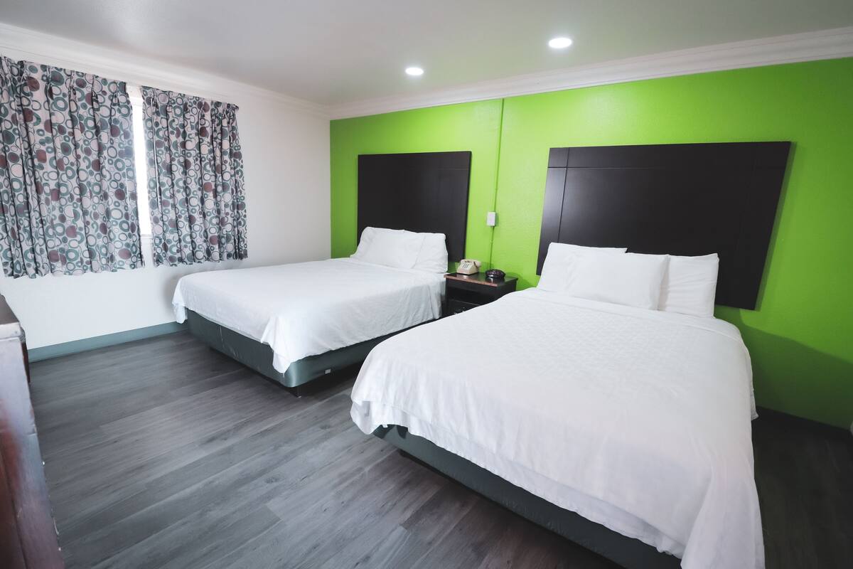 A hotel room with two beds, a green accent wall, and a patterned curtain.