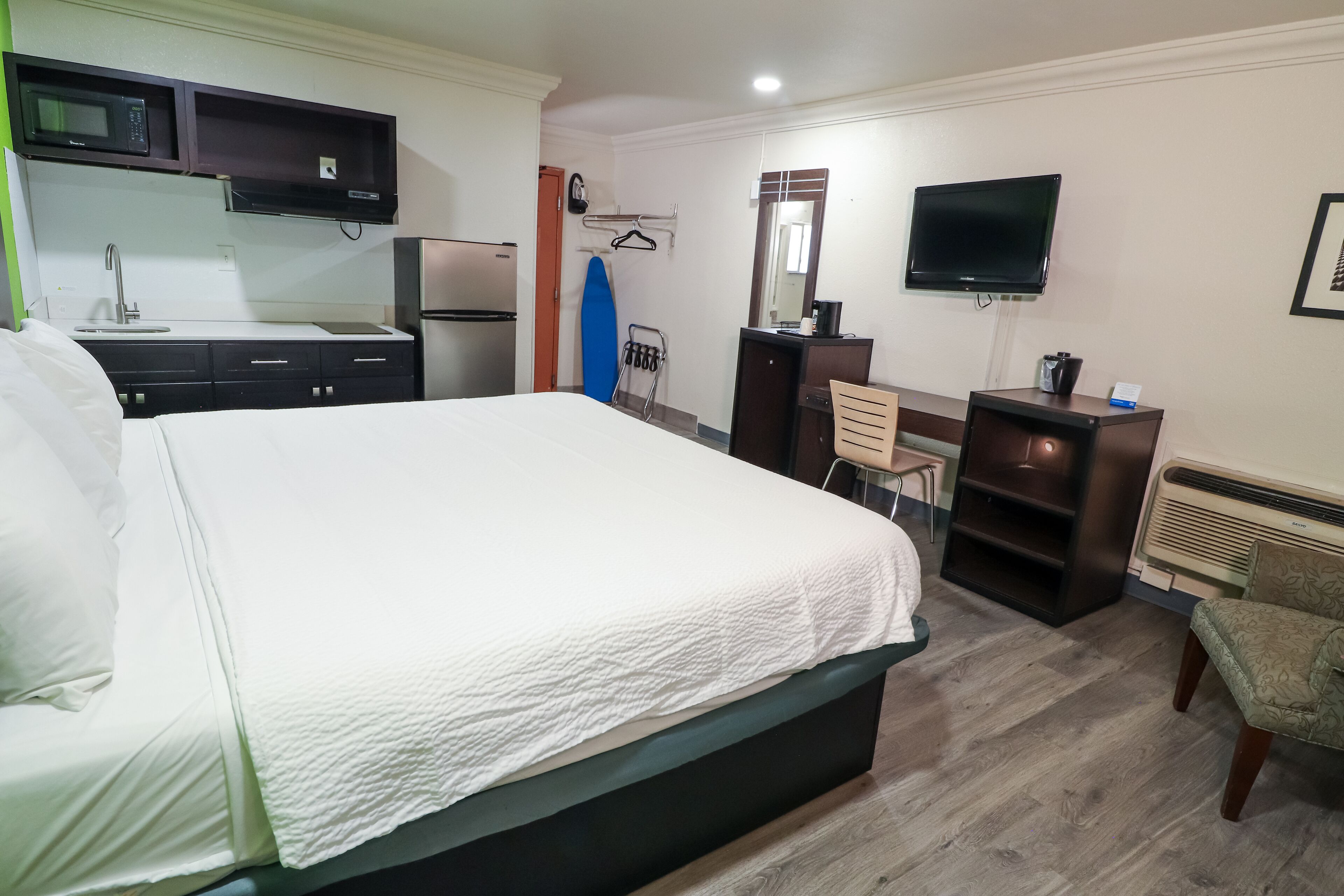 A hotel room with a bed, a desk, a chair, a TV, a microwave, a refrigerator, and a heater.