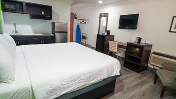 A hotel room with a bed, a desk, a chair, a TV, a microwave, a refrigerator, and a heater.