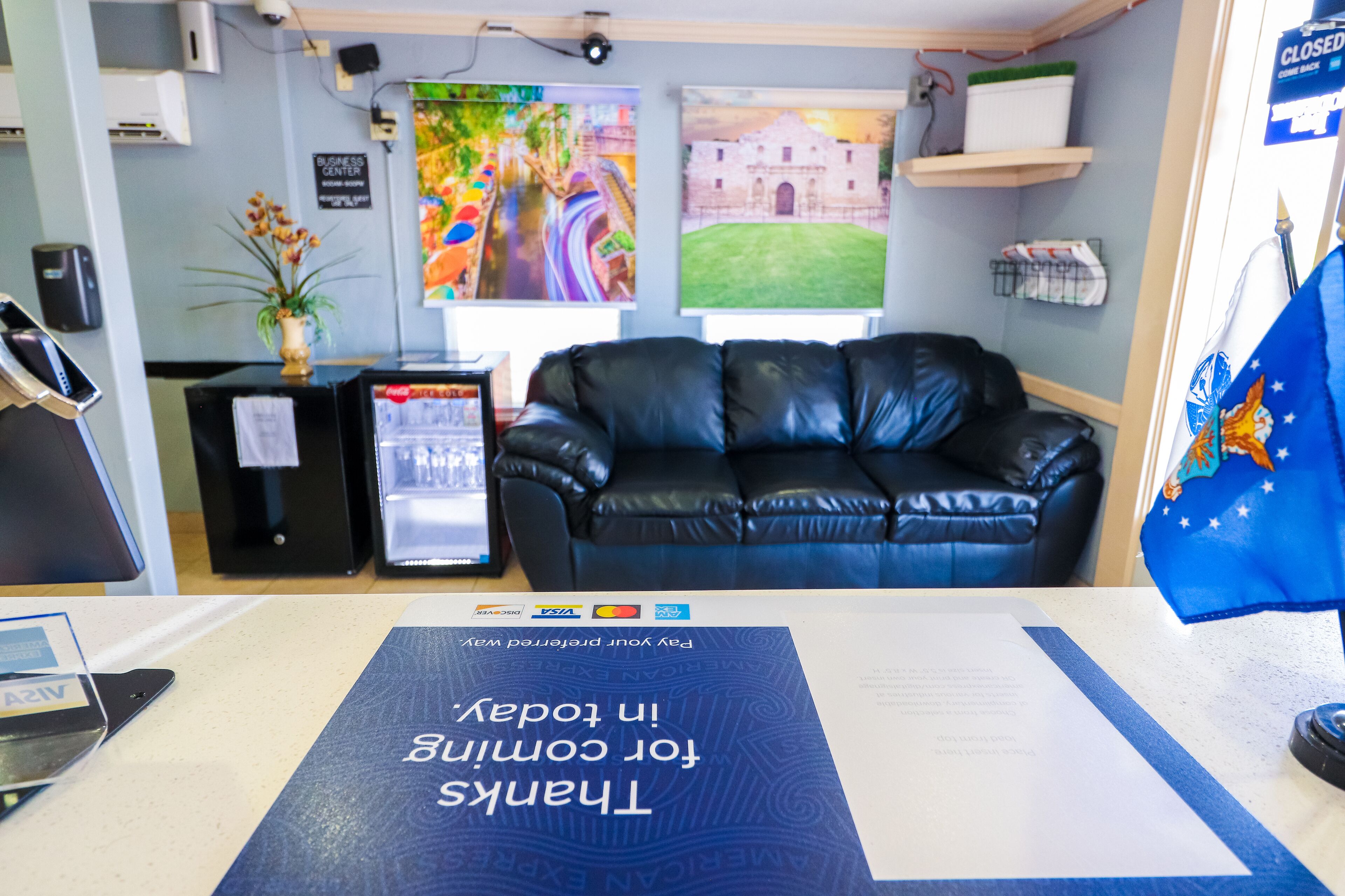 Un área de recepción con un sofá de cuero negro, un escritorio con computadora, una bandera y un letrero que dice 