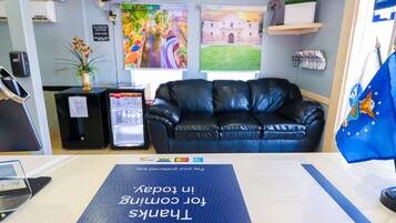 Un área de recepción con un sofá de cuero negro, un escritorio con computadora, una bandera y un letrero que dice