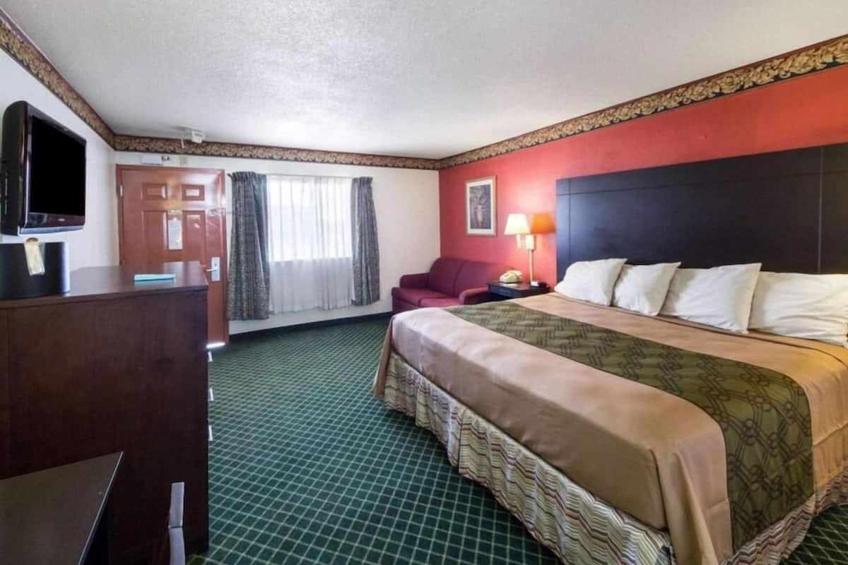 A hotel room with a bed, a desk, a television, a chair, and a window with curtains.