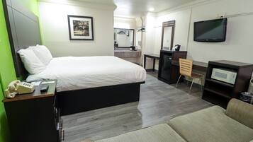 Quarto de hotel com cama, escrivaninha, televisão, micro-ondas e uma cadeira.