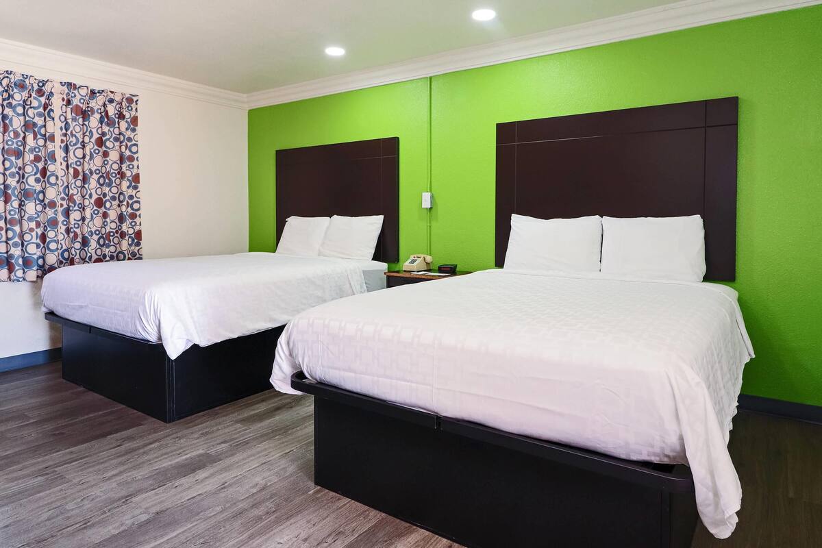 A hotel room with two beds, green walls, and a patterned curtain.