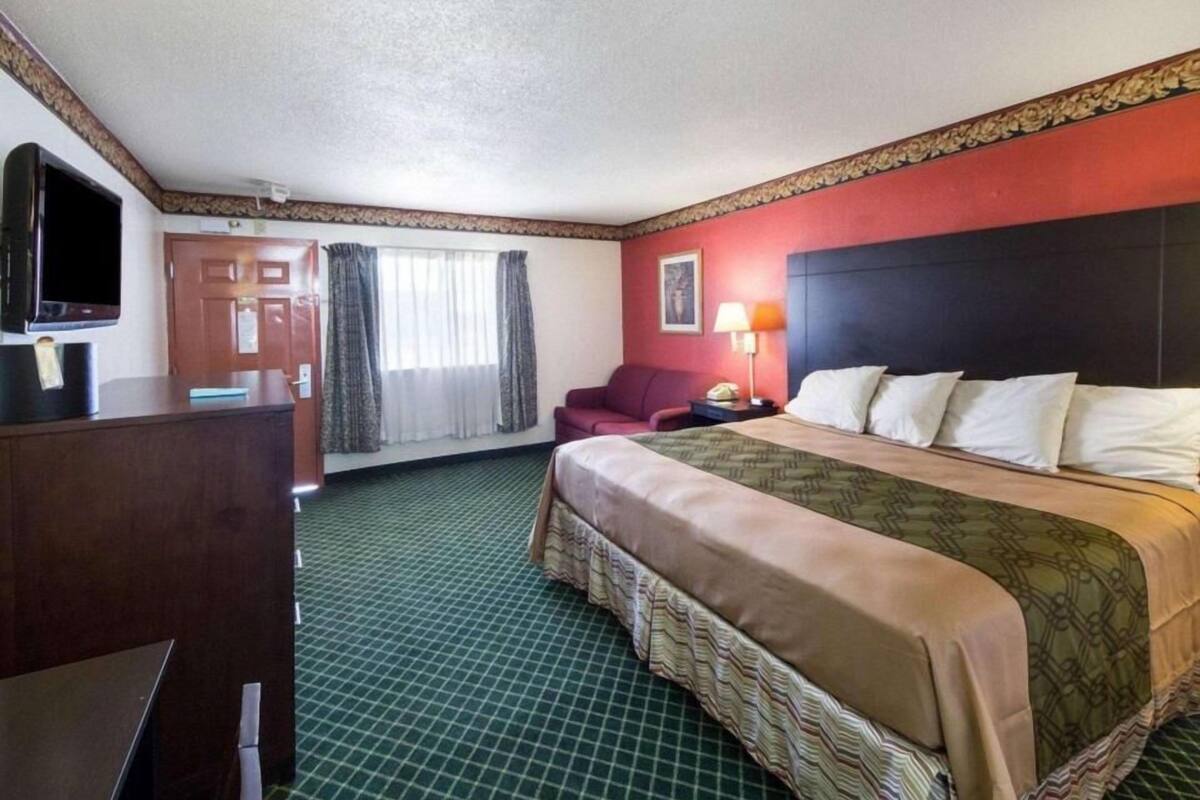 A hotel room with a bed, a desk, a television, a chair, and a window with curtains.