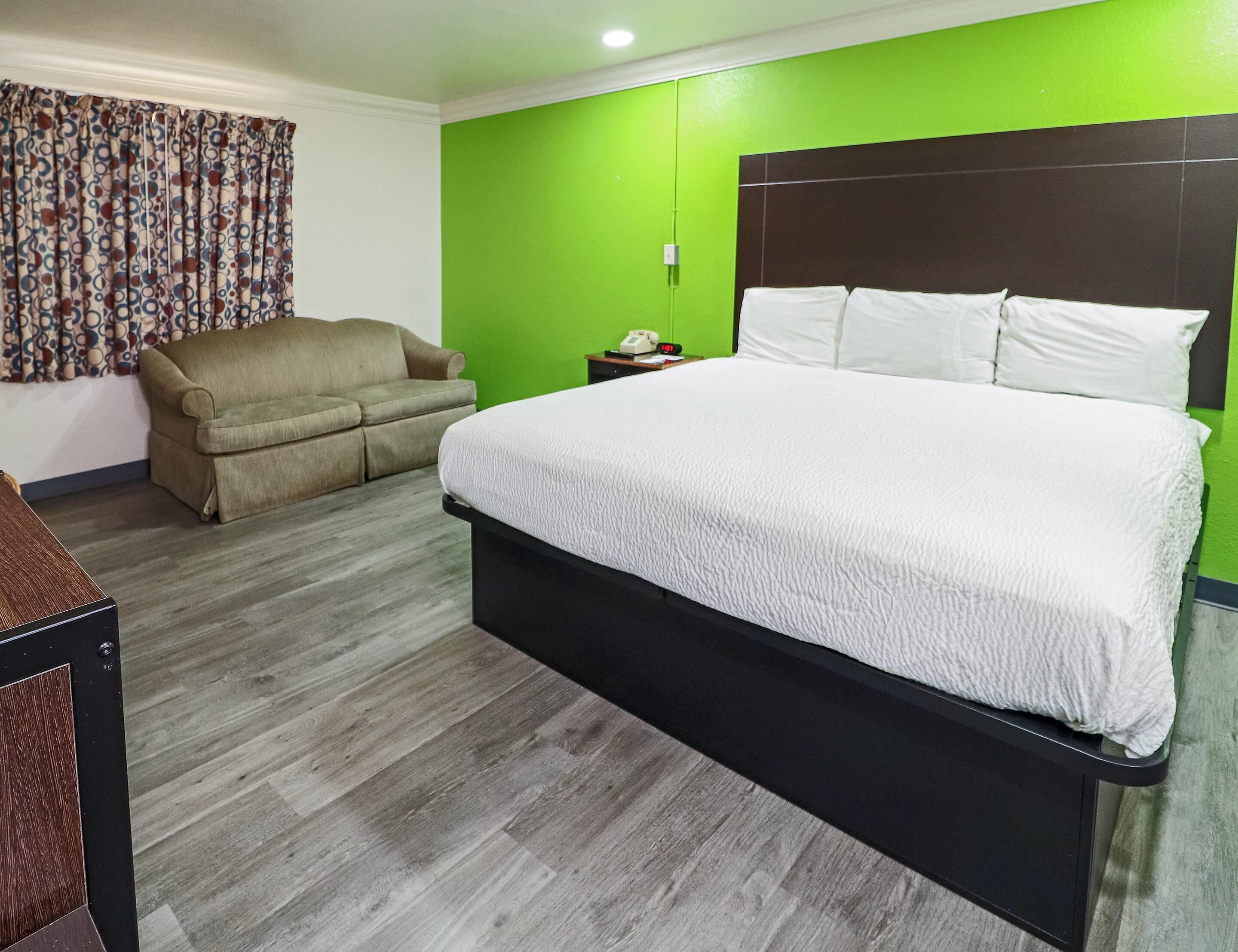 A hotel room with a large bed, a sofa, a bedside table with a phone, and a green accent wall.