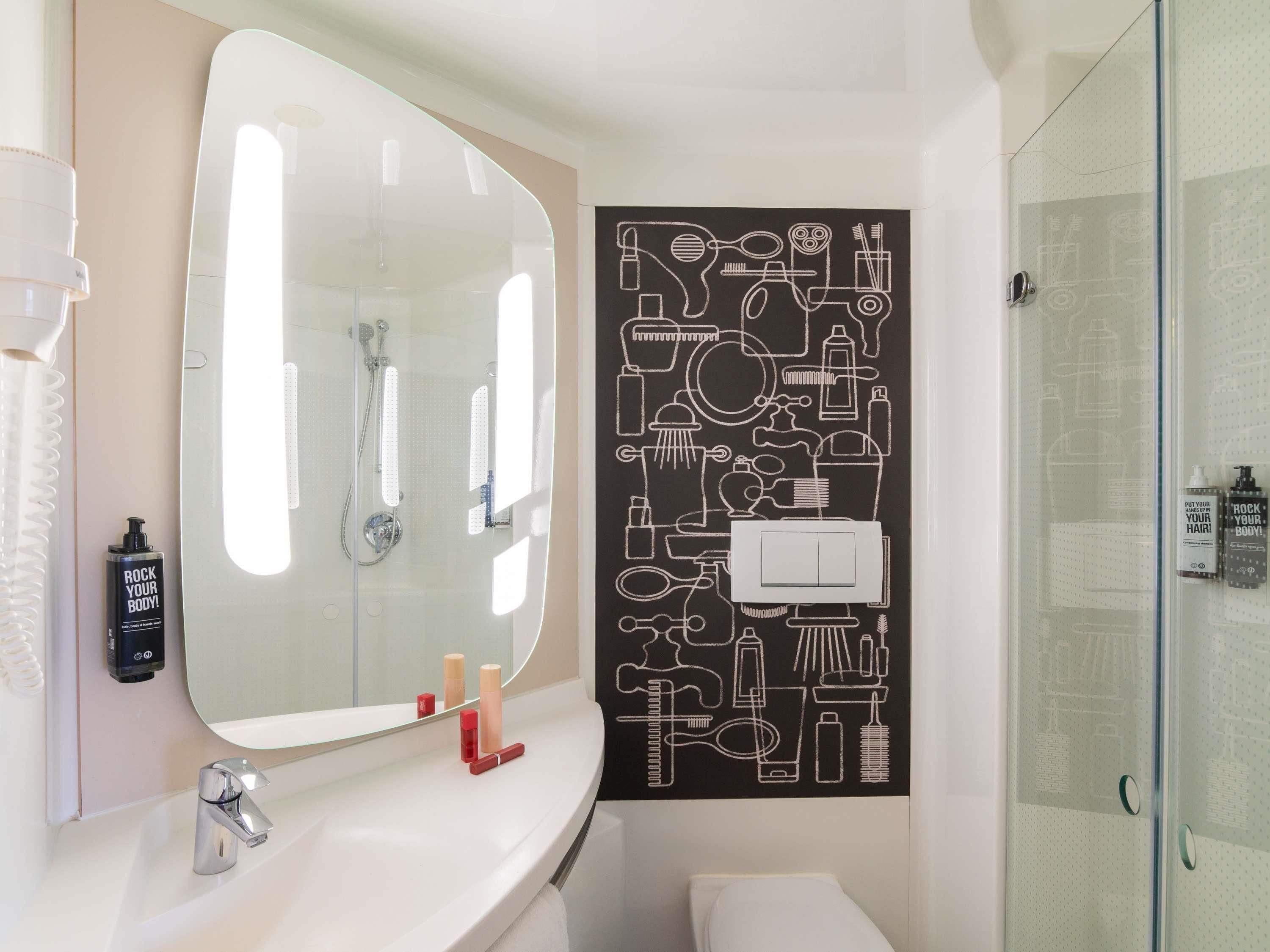 Un baño con un espejo grande, un lavamanos con artículos de aseo y una ducha.