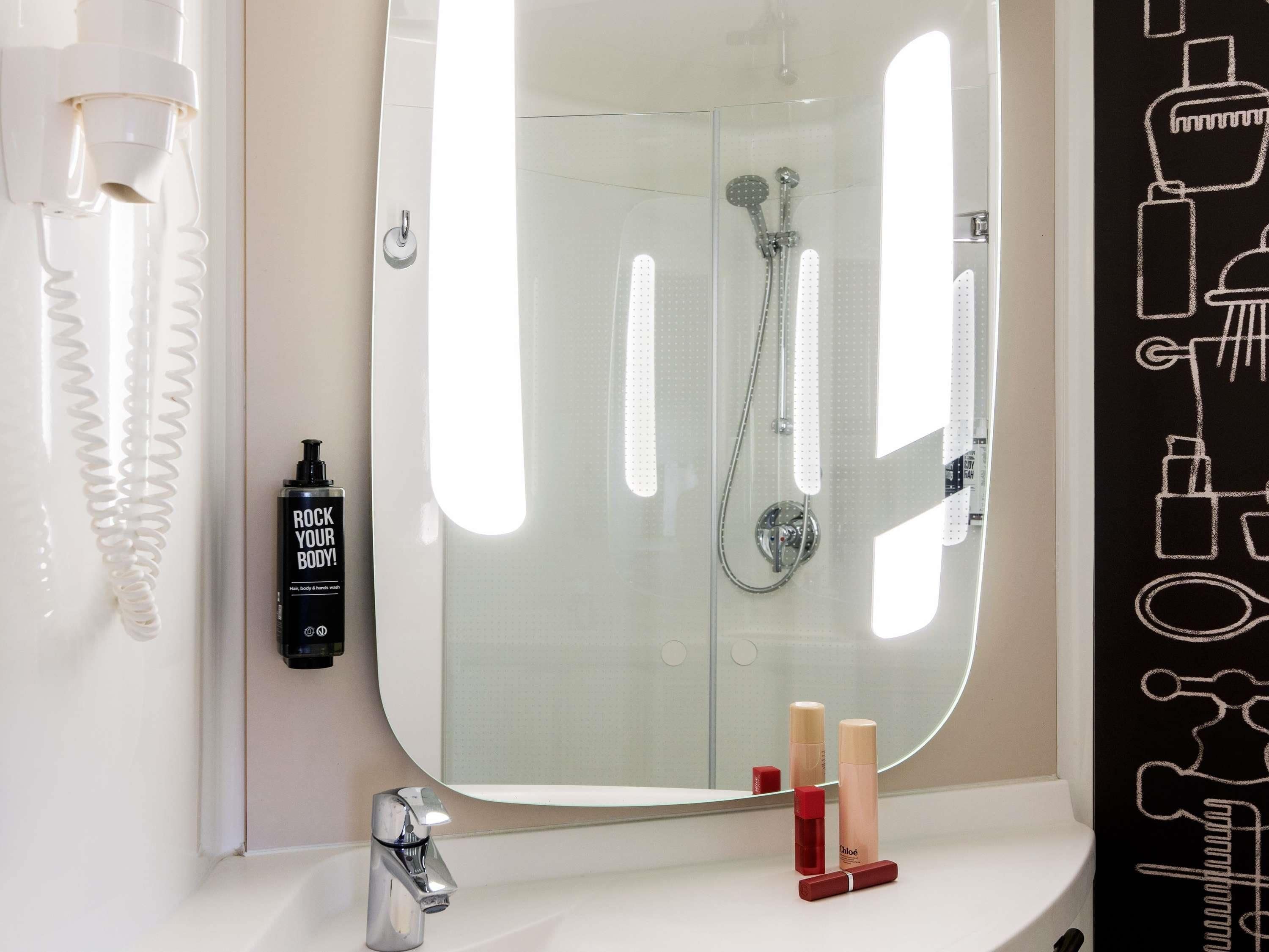 A bathroom with a large mirror, a shower with a handheld showerhead, and a sink with a faucet.