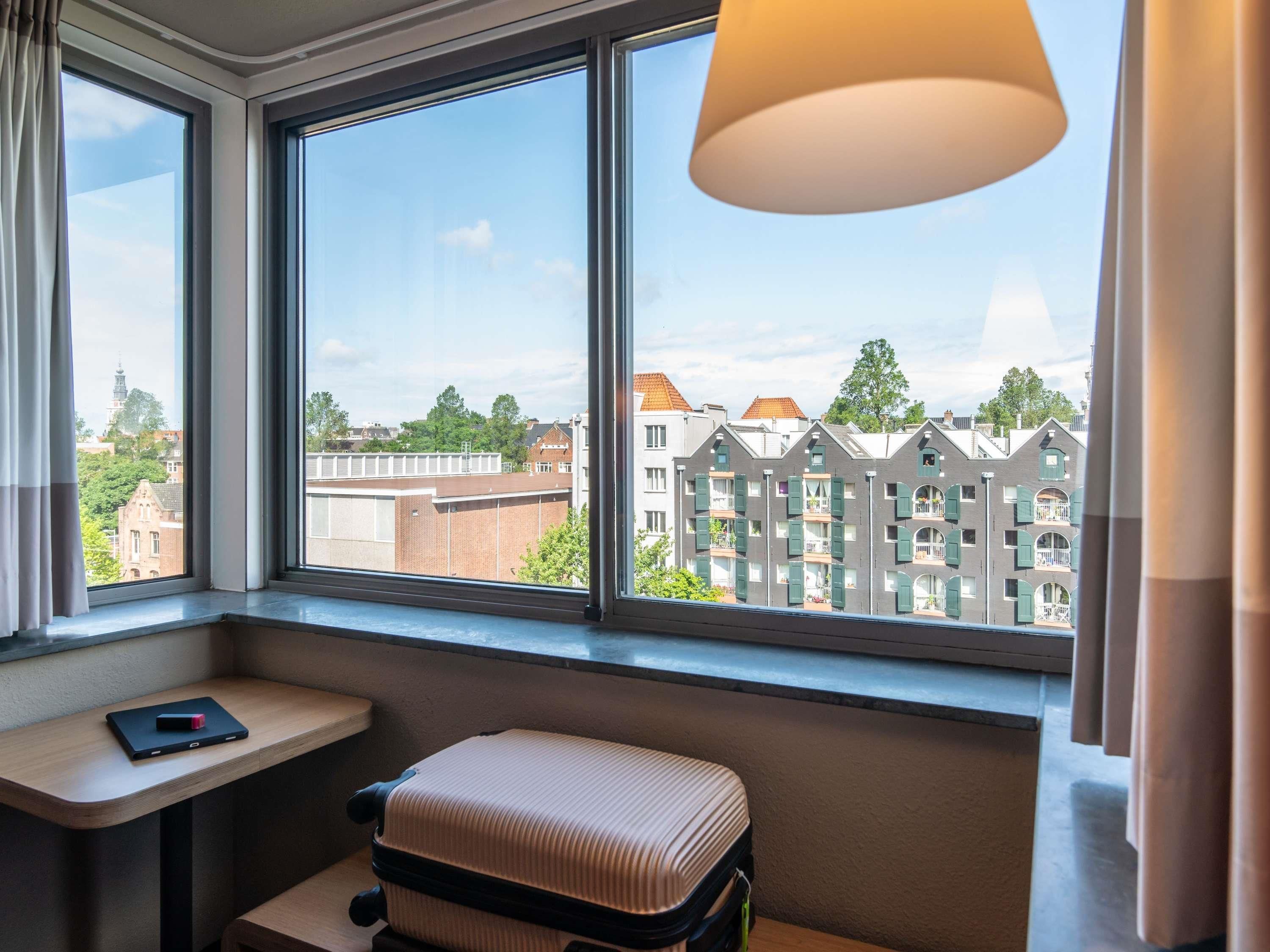 A room with a window, a desk, a chair, and a suitcase.