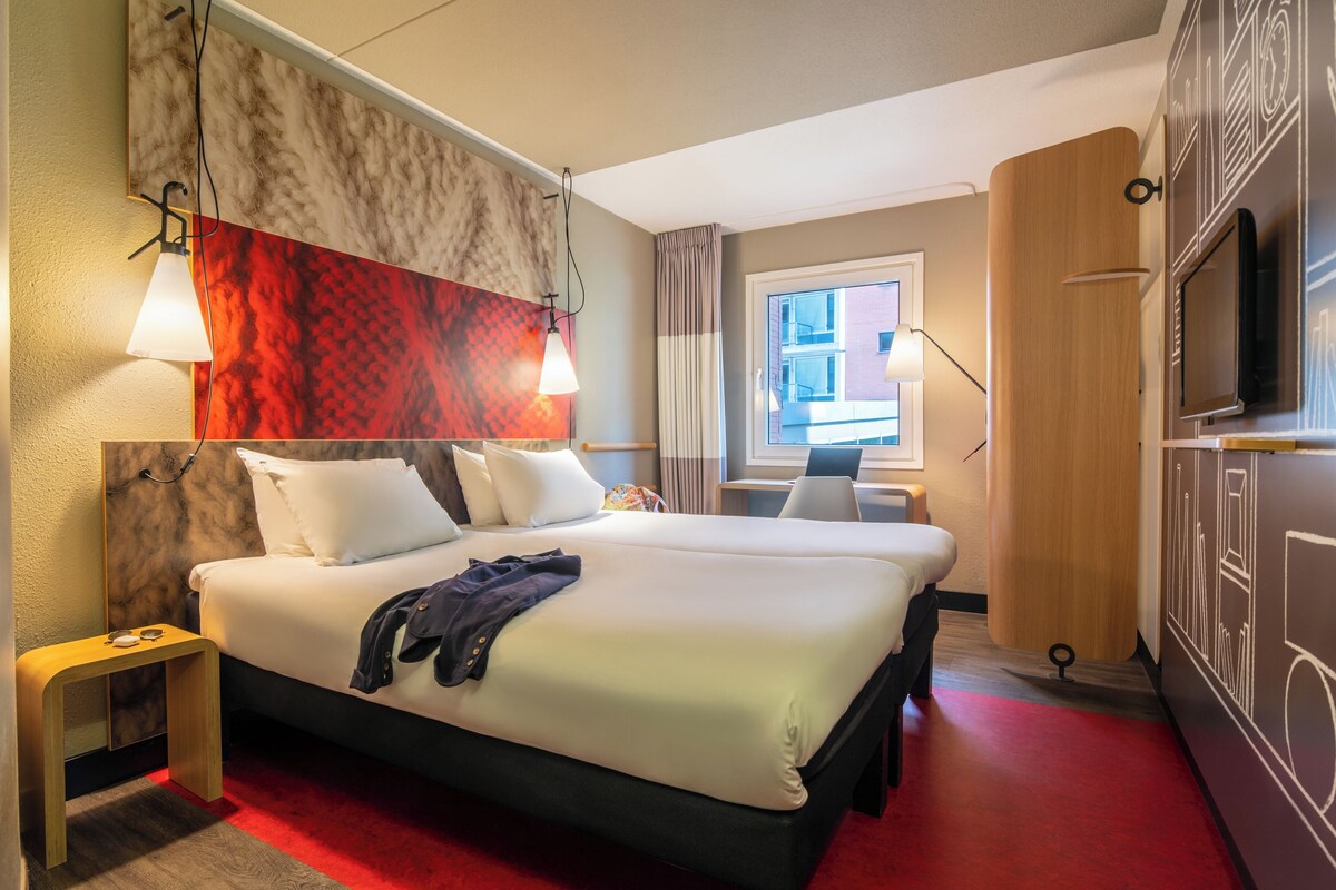 A hotel room with a large bed, bedside tables, a TV, and a window with curtains.