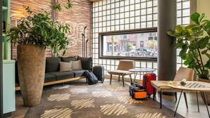 Rebedor d'hotel modern amb una gran planta en test, un sofà, una taula petita i una finestra amb vista al carrer.