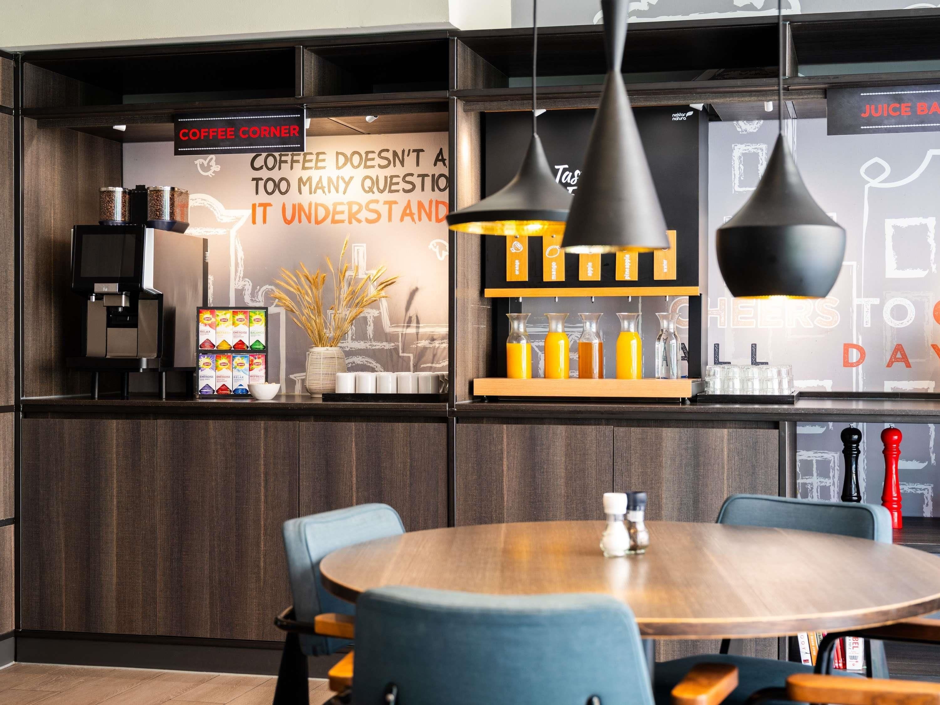 A modern coffee bar with a sign stating 'Coffee doesn't a too many question it understand,' a coffee machine, and a selection of beverages.