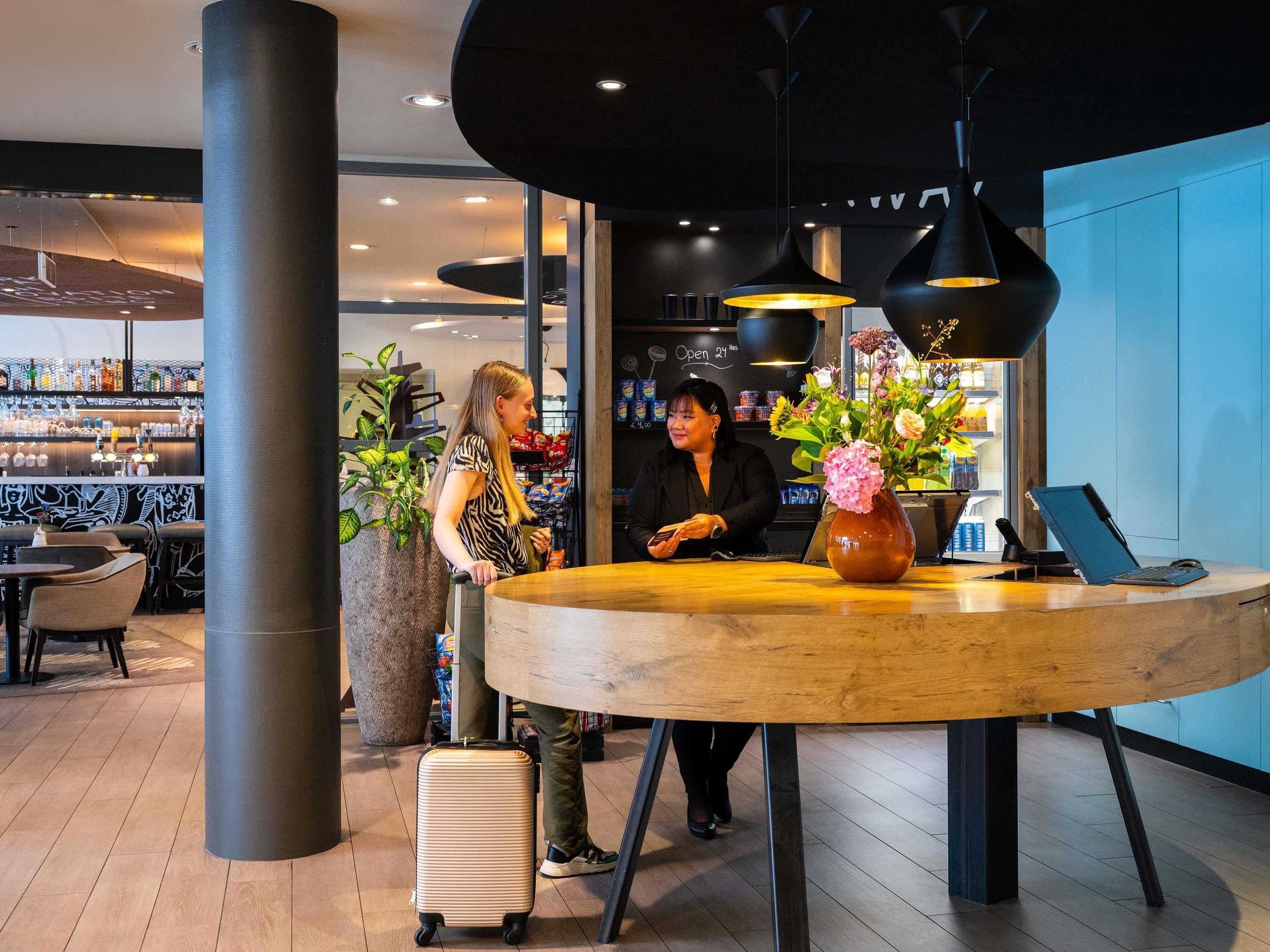 A reception desk with a laptop, a vase with flowers, and a bar area in the background.
