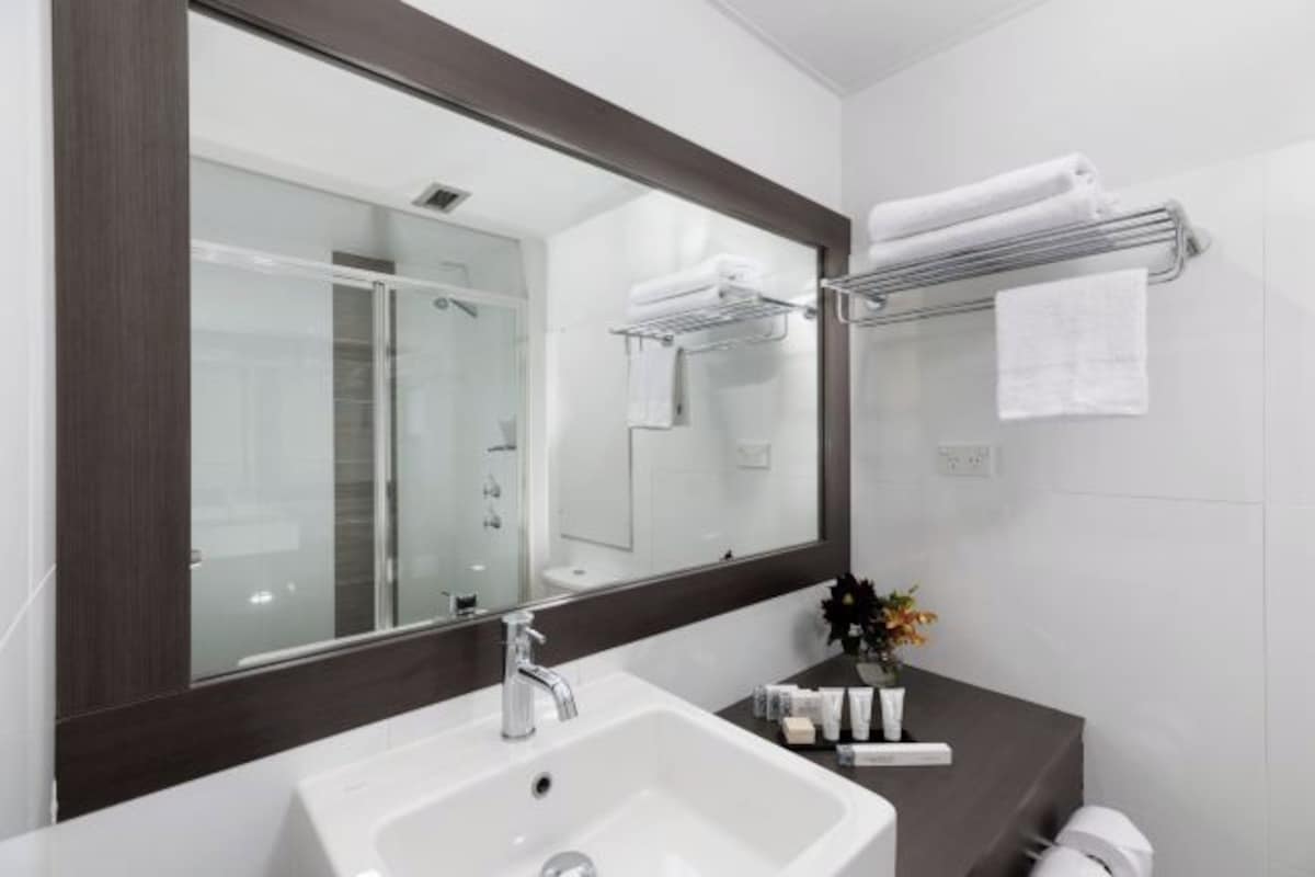 A modern bathroom with a large mirror, white sink, and towel rack.