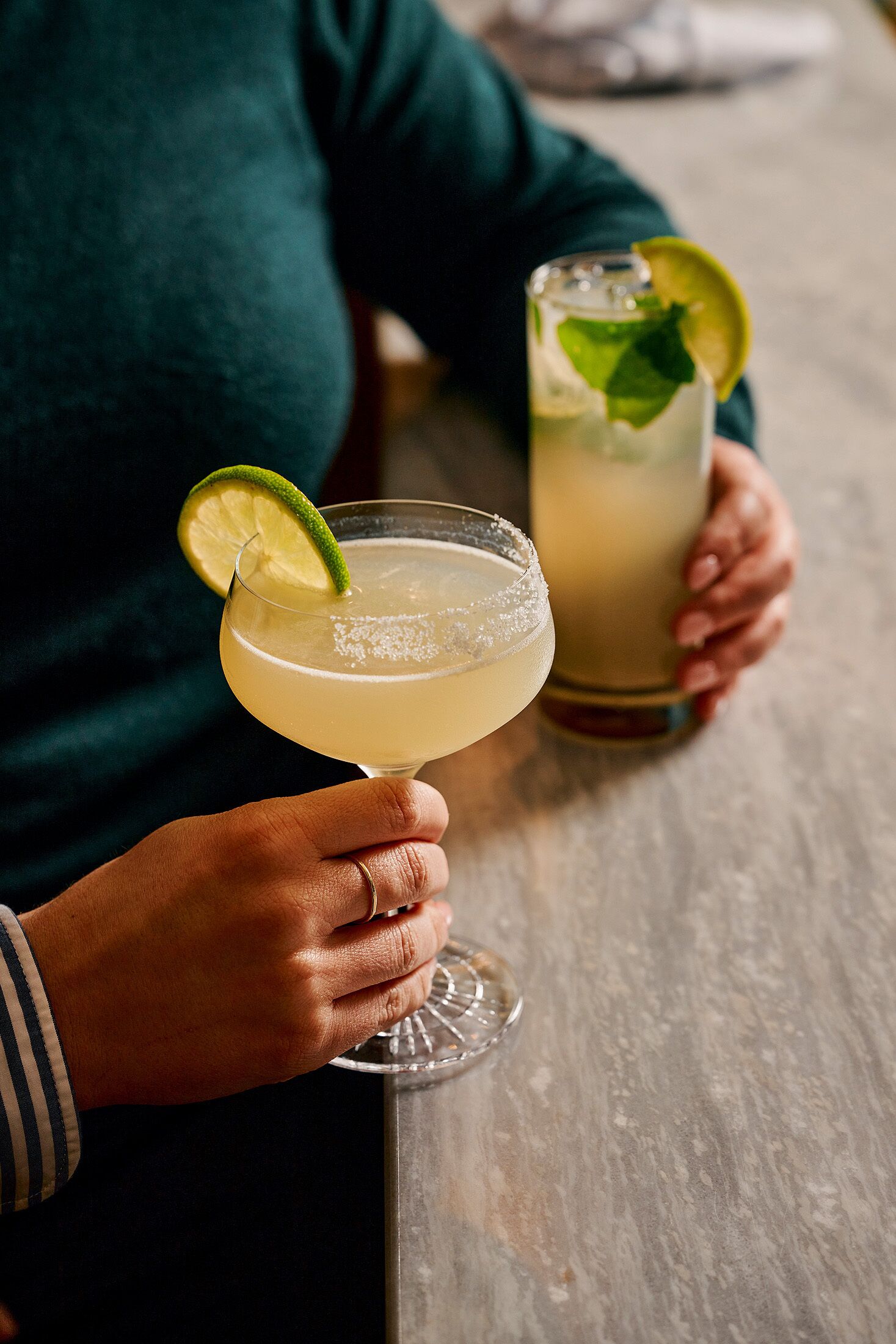 A person holding a margarita glass with a lime garnish.