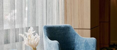 A modern room with a blue armchair, a round table with a vase, and a wooden cabinet.