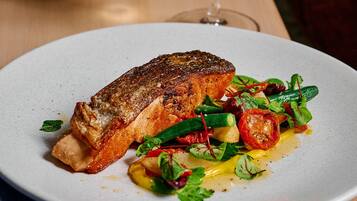 Ein Teller mit Essen, darunter Lachs, Gemüse und ein Glas Weißwein auf einer Holztischplatte.