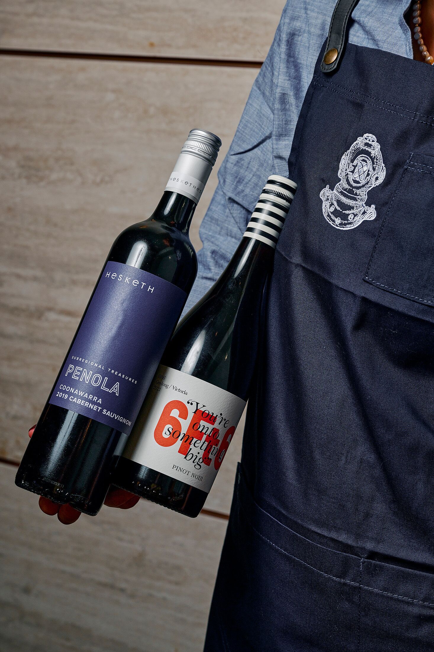 A person holding two wine bottles, one labeled 'Penola' and the other '6 Big'.