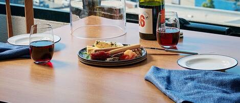 Une table à manger avec une bouteille de vin, un verre de vin rouge, un verre d’eau, une assiette de nourriture et un récipient transparent en verre.