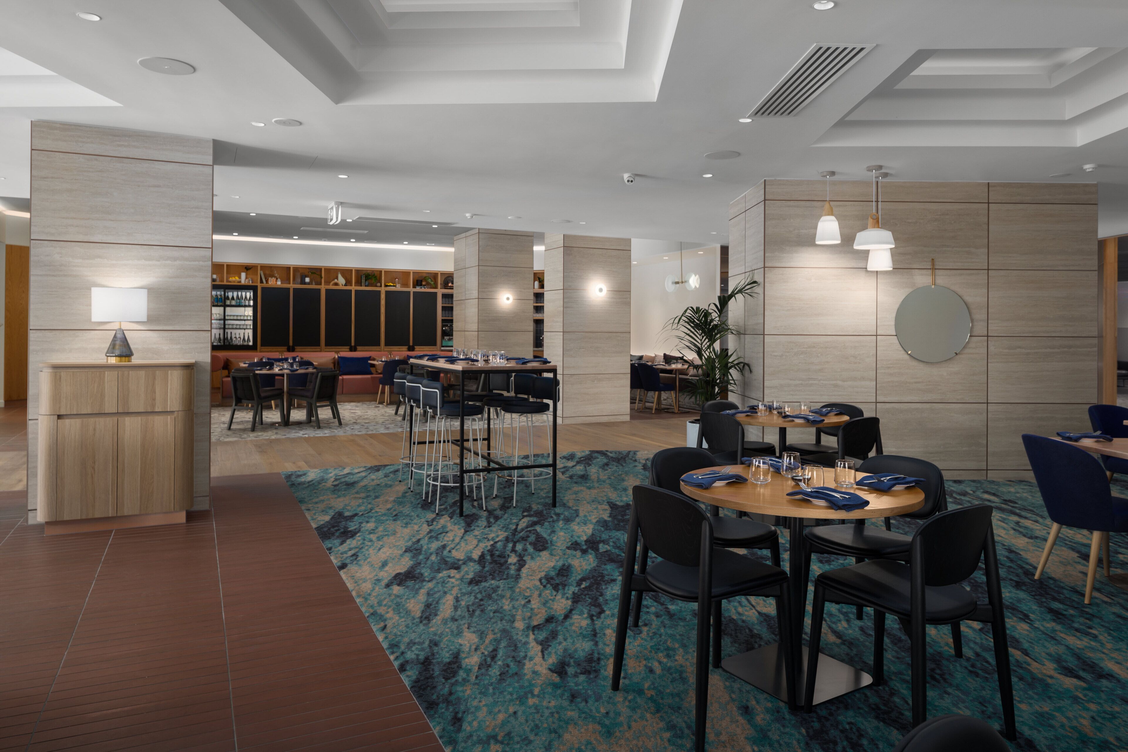 Un hall d’hôtel moderne comprenant un comptoir d’accueil, des espaces de détente et un bar.