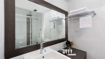 A modern bathroom with a large mirror, a white sink, and a glass-enclosed shower.