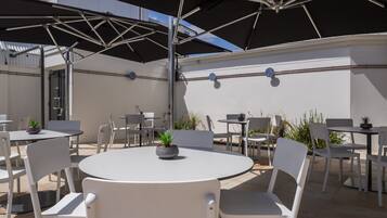 A patio area with round tables and white chairs, some with umbrellas.