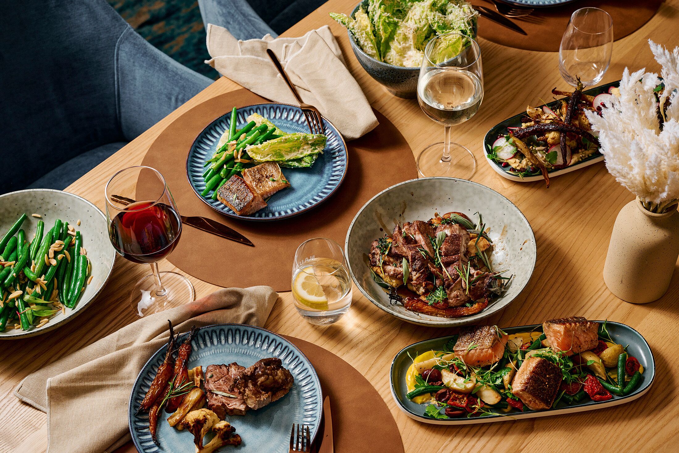 A dining table with various dishes, glasses of wine, and a vase with white flowers.