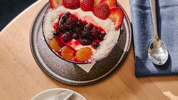 A dessert plate with strawberries and berries, a cup of coffee with latte art, and a spoon on a napkin on a wooden table.
