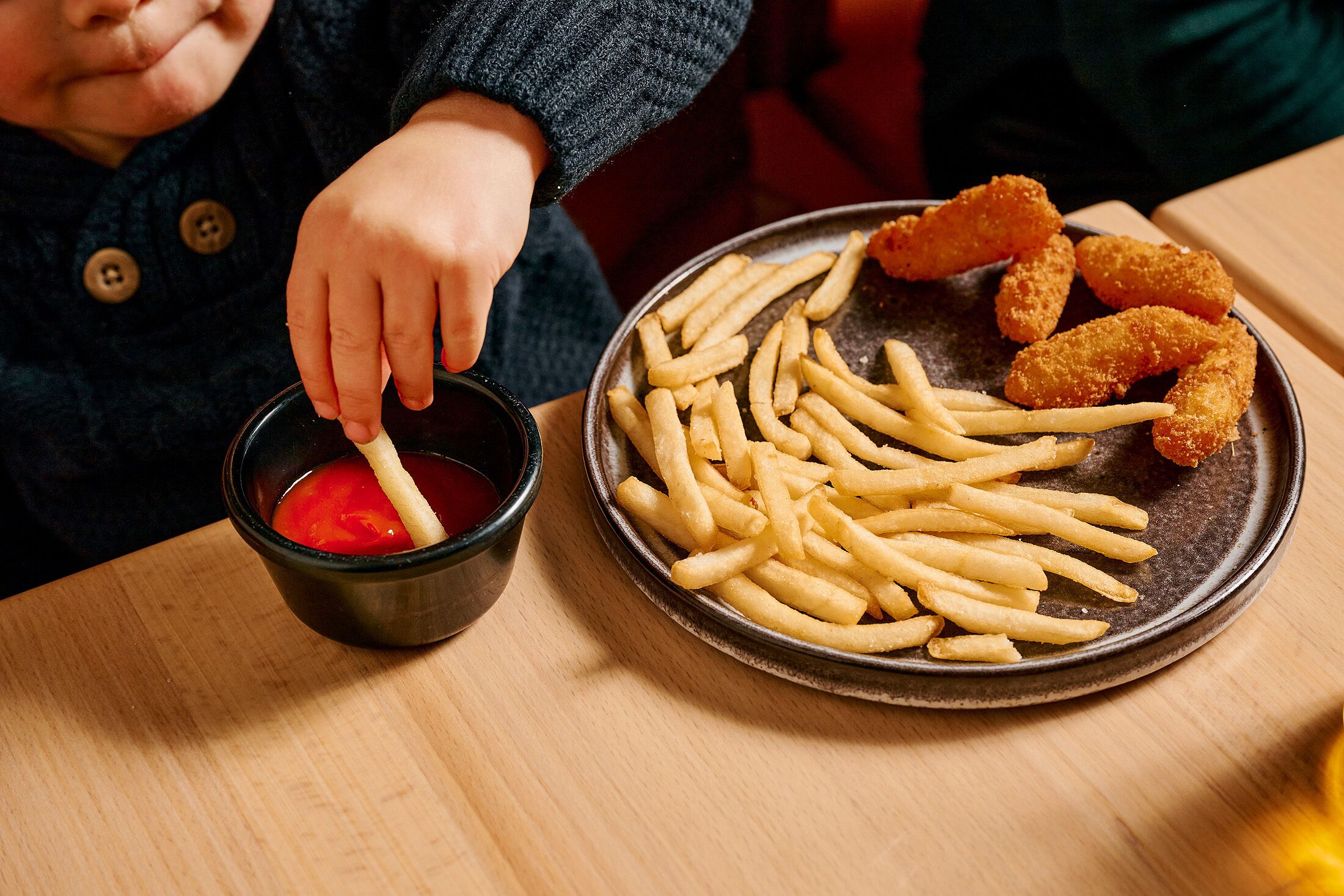 Ein Teller mit Pommes Frites und panierten Hähnchenstreifen mit Ketchup.