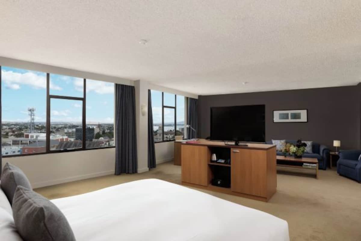 A hotel room with a large bed, a TV, a desk, and a view of the city.