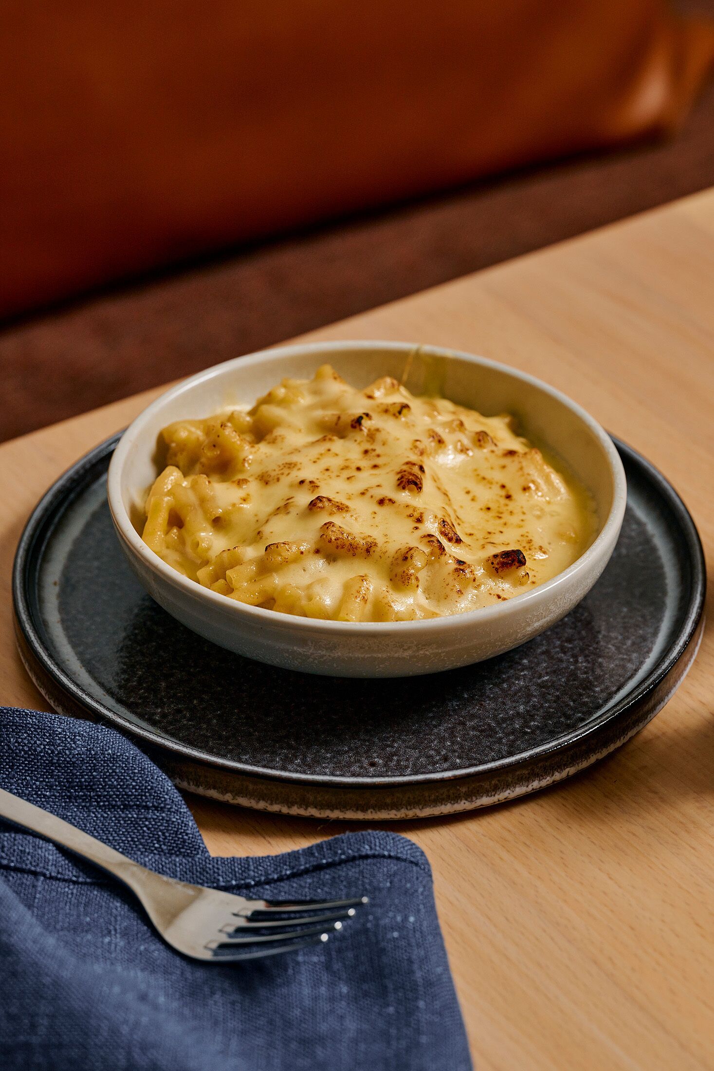 Een kom macaroni met kaas op een donker bord, met een vork ernaast.