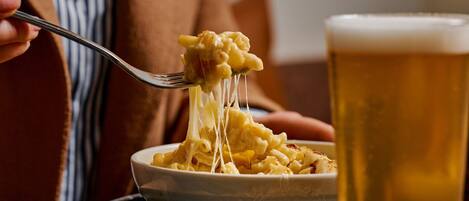 Un plato de macarrones con queso, con un tenedor levantando una porción, y un vaso de cerveza al lado.