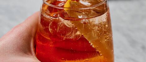 A hand holding a glass of red drink with a cherry garnish.