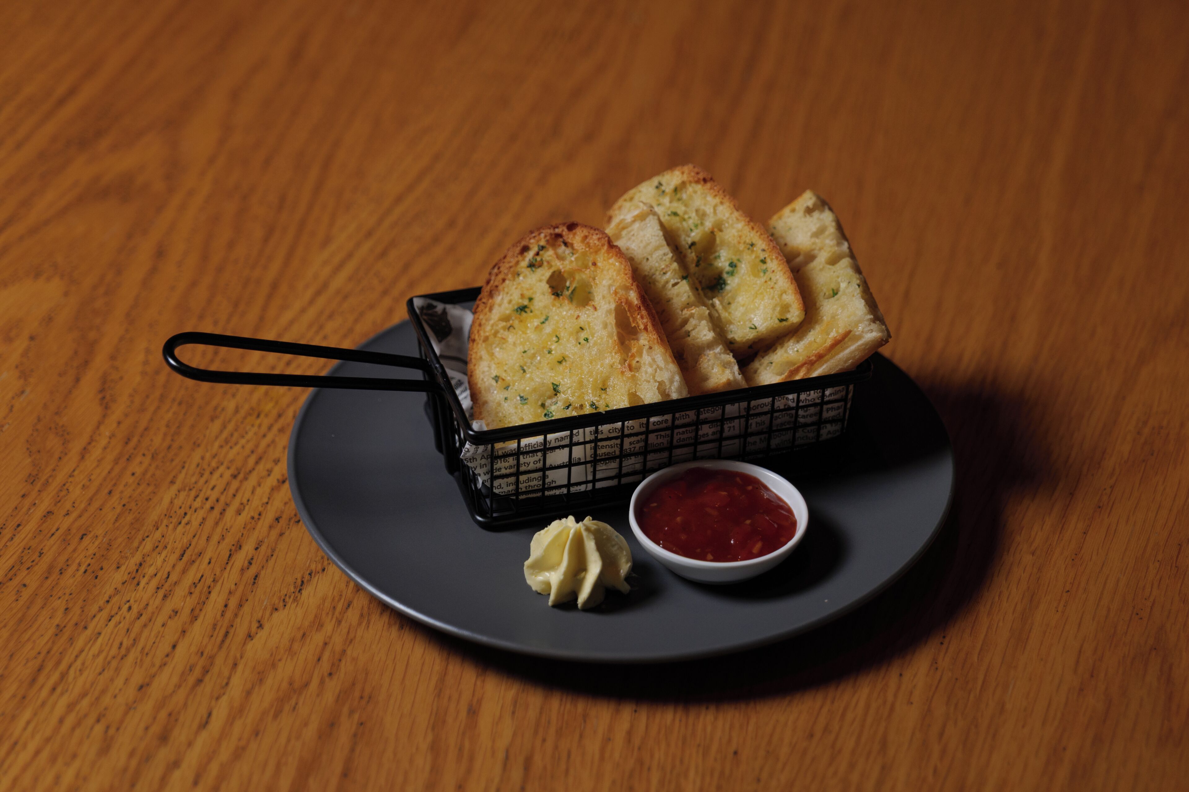 Una cesta de pan con ajo sobre un plato con un recipiente pequeño de salsa.
