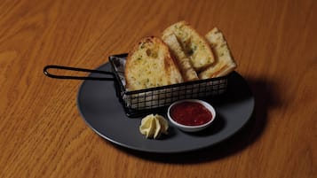 Una cesta de pan con ajo sobre un plato con un recipiente pequeño de salsa.