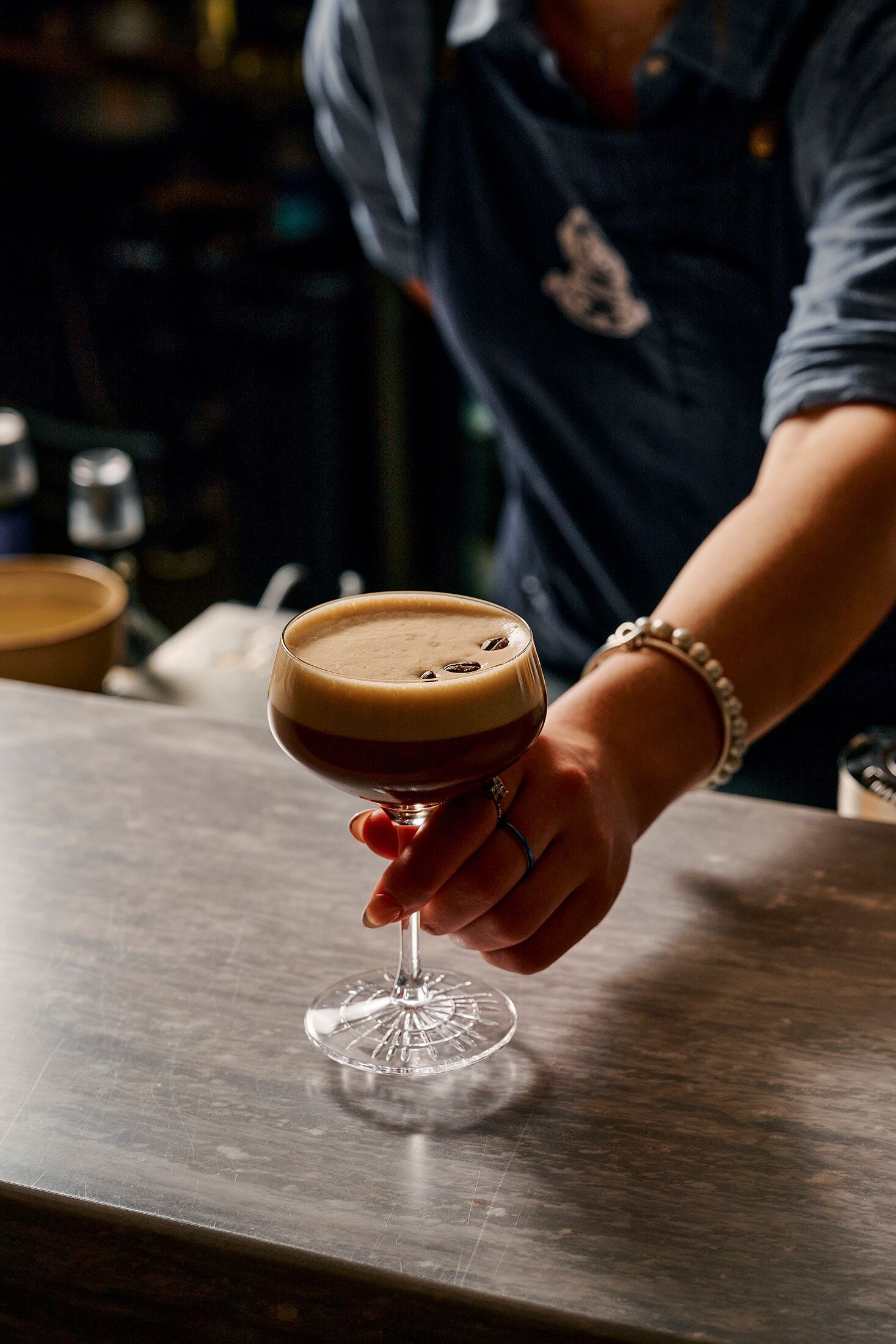 A hand holding a cocktail glass with a layered drink on a bar counter.