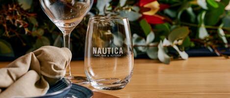 Two clear glass wine glasses with the text "NAUTICA POOL BAR & KITCHEN" on one.