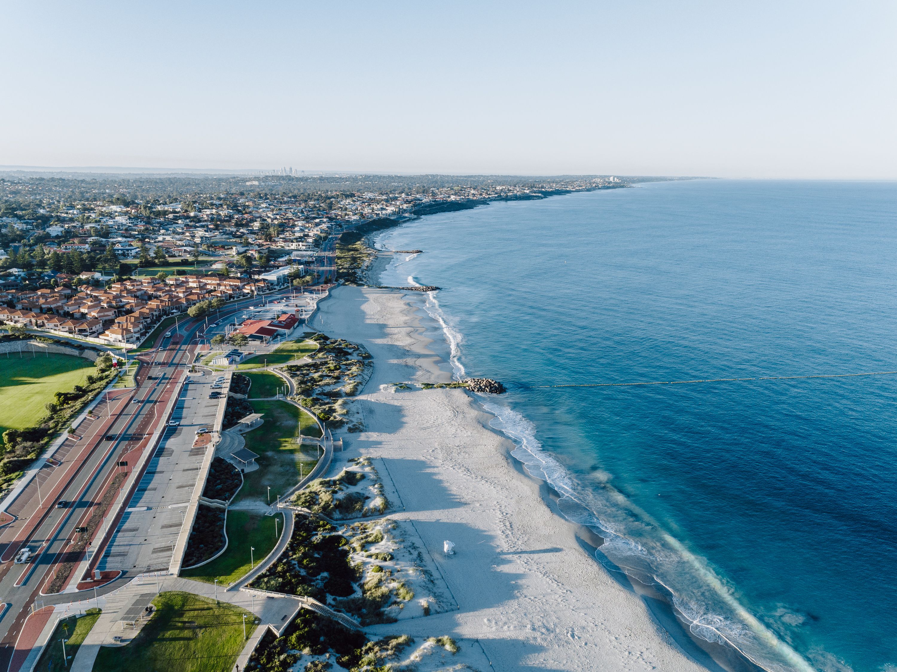 Vista aérea de una ciudad costera con playa, carreteras y zonas residenciales.