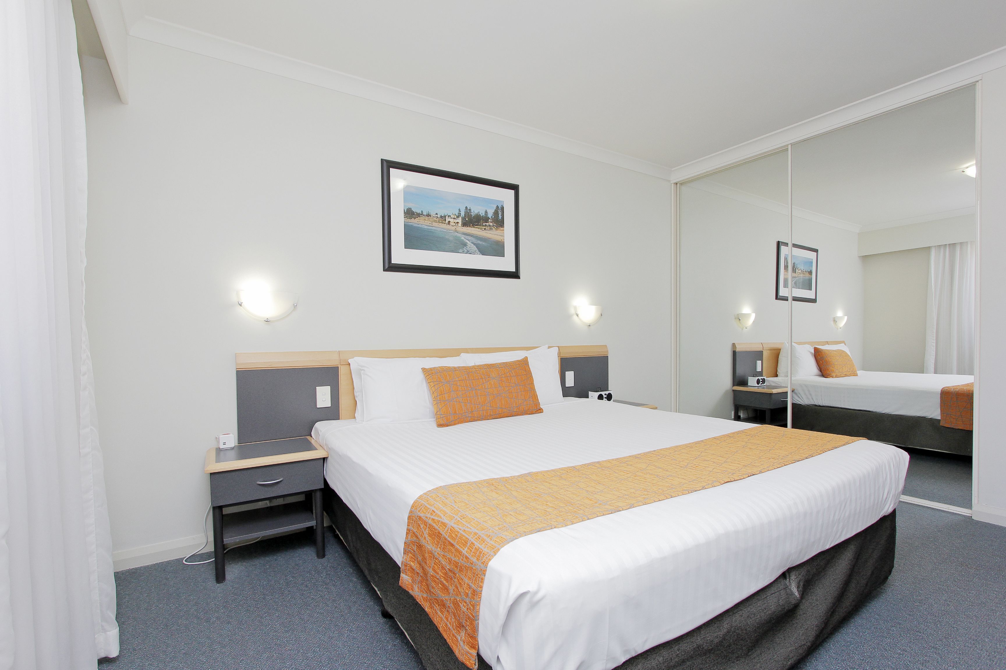 A hotel room with a large bed, a bedside table, a nightstand, a mirror, and a picture on the wall.